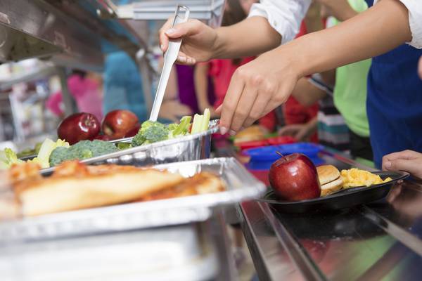 Cafeteria worker helping elementary students select food in lunch line