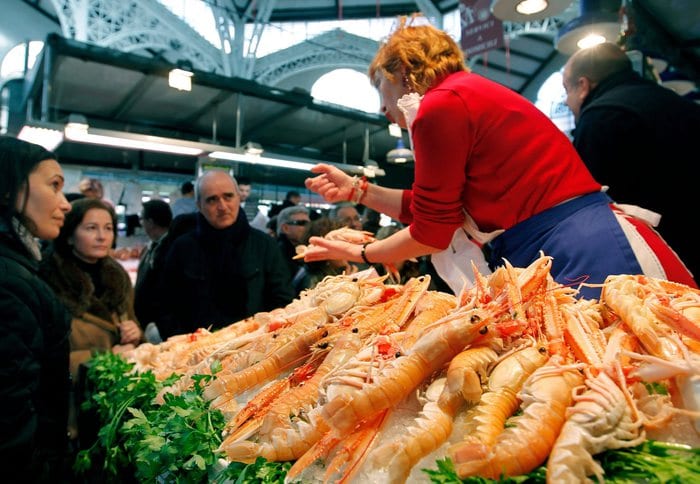 epa03045977 A Spanish vendor selling seafood chats with customers at her stall in a public market in Valencia, eastern Spain, 31 December 2011. Hundreds of people have packed the grocery shops to do last-minute shopping before the New Year dinner.  EPA/JUAN CARLOS CARDENAS