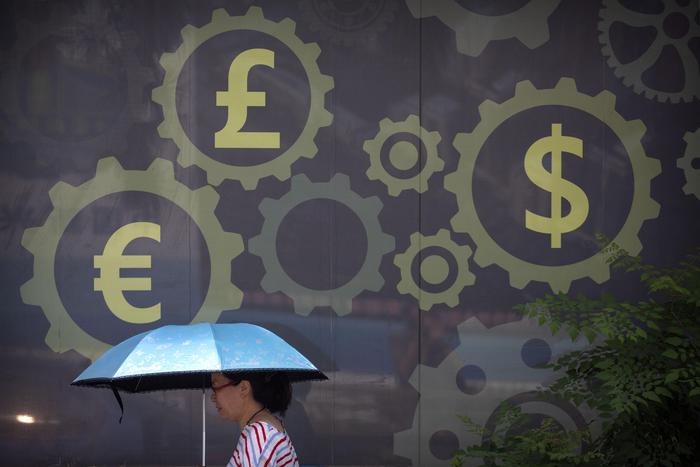 In this July 20, 2018, photo, a woman carries an umbrella as she walks past a mural displaying world currency symbols outside of a bank in Beijing. China lowered the trading range for its currency for a fourth day on Thursday, Aug. 8, 2019, showing its potential for use as a trade weapon against Washington, but the exchange rate steadied following declines that alarmed financial markets. (ANSA/AP Photo/Mark Schiefelbein) [CopyrightNotice: Copyright 2018 The Associated Press. All rights reserved]