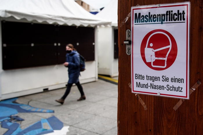 epa08824094 A woman walks next to a sign informing customers to wear face masks as she passes by a closed Christmas Market stall at Potsdamer Platz in Berlin, Germany, 16 November 2020. Effective from 02 November, Germany is on nationwide restrictions to prevent a further explosion in the number of corona infections, such as closing bars and restaurants for a month.  EPA/FILIP SINGER