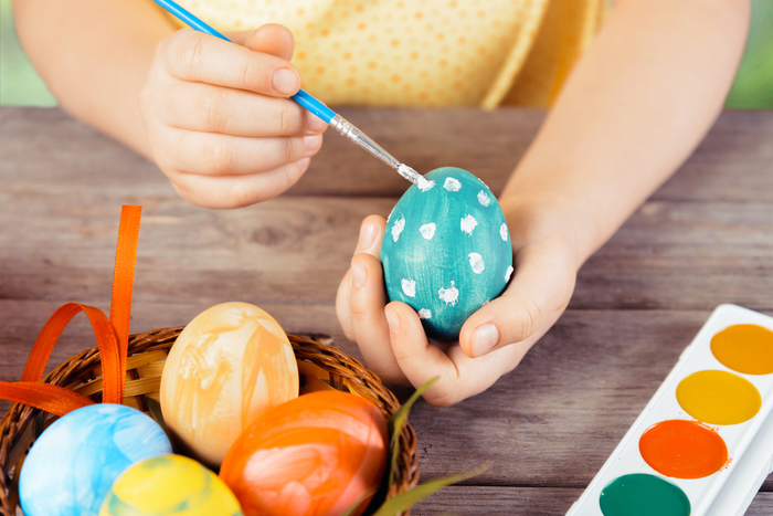 Child hands paint egg for Easter on a wooden table