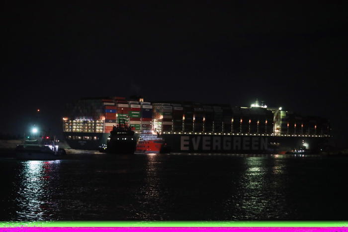 epa09101904 Night scene of the Ever Given container ship which ran aground in the Suez Canal, Egypt, 27 March 2021. The Ever Given, a large container ship ran aground in the Suez Canal on 23 March, blocking passage of other ships and causing a traffic jam for cargo vessels. The head of the Suez Canal Authority announced that 'the navigation through the Suez Canal is temporarily suspended' until the floatation of the Ever Given is completed. Its floatation is being carried out by eight large tugboats that are towing and pushing the grounding vessel  EPA/KHALED ELFIQI