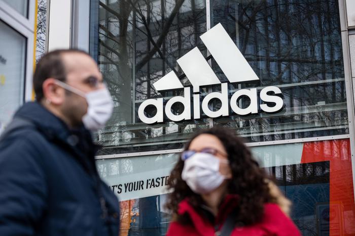 epa08334151 A man and a woman with protective mask stand in front of adidas store with the logo of the sporting goods manufacturer, in Berlin, Germany, 31 March 2020. The German government and local authorities are heightening measures to stem the spread of the coronavirus SARS-CoV-2 which causes the Covid-19 disease.  EPA/JENS SCHLUETER