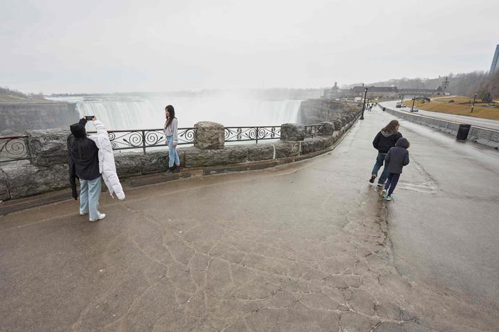 Tourists take photos in front of the Horseshoe Falls, nearly empty due to travel bans and concerns over Covid-19 in Niagara Falls, Ontario, on March 18, 2020. - US and Canada have mutually agreed on March 18, 2020 to temporarily restrict 