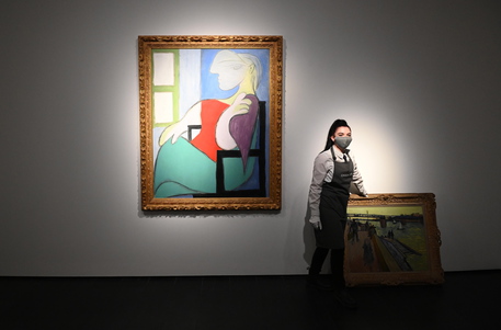 epa09152194 Art handlers pose with the works 'Le pont de Trinquetaille' by Vincent Van Gogh (R) and 'Femme assise pres d'une fenetre (Marie-Therese)' by Pablo Picasso (R) at a media preview at Christies auction house in London, Britain, 22 April 2021. The 20th Century Evening Sale takes place in New York on 13 May 2021.  EPA/NEIL HALL