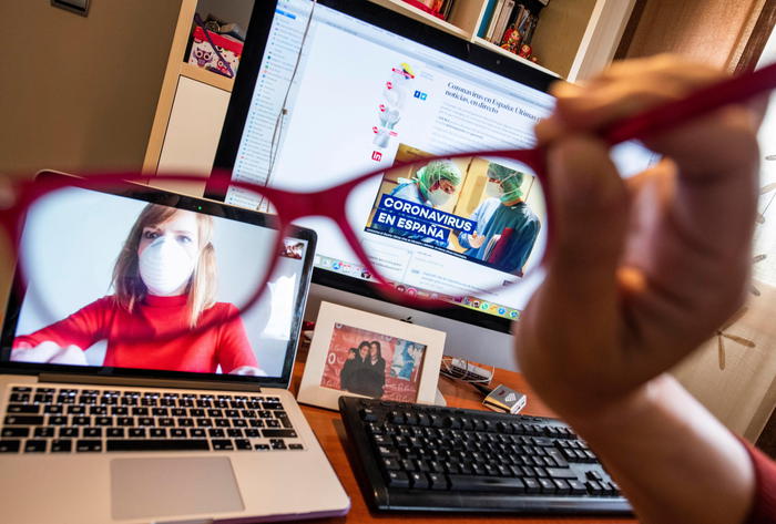epa08352524 Maria Ruiz (unseen) puts her glasses on in front of her laptop and a computer as she works at home in Granada, southern Spain, 09 April 2020. Mobile phones, tablets, computers and TVs are the windows to the world, amid the lockdown caused by coronavirus outbreak, but its use could involve additional risks for vision, doctors alerted recently. Spain faces the 26th consecutive day of mandatory home confinement in a bid to slow down the spread of the pandemic COVID-19 disease caused by the SARS-CoV-2 coronavirus.  EPA/Miguel Angel Molina