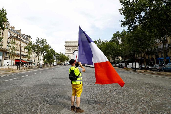 A protester, wearing a yellow vest, waves a national flag on the Champs Elysees avenue on the sidelines of a demonstration against the compulsory vaccination for certain workers and the mandatory use of the health pass called by the French government in Paris on July 24, 2021. - Since July 21, people wanting to go to in most public spaces in France have to show a proof of Covid-19 vaccination or a negative test, as the country braces for a feared spike in cases from the highly transmissible Covid-19 Delta variant. (Photo by Sameer Al-DOUMY / AFP)
