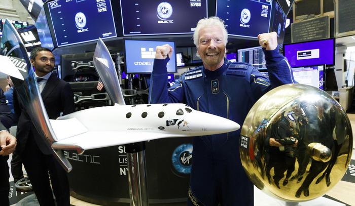 epa07956379 ]Sir Richard Branson (C), the founder of Virgin Galactic, poses with a ceremonial bell and a spaceship model at the New York Stock Exchange to celebrate the first day of trading of Virgin Galactic Holdings shares in New York, New York, USA, on 28 October 2019. The commercial space travel and exploration company is a result of the merger of Virgin Galactic and Social Capital Hedosophia.  EPA/JUSTIN LANE