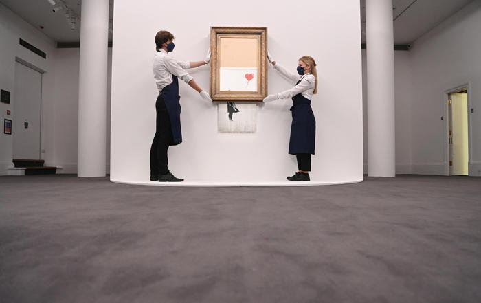 epa09445070 Gallery employees pose for photographers next to a painting entitled 'Love is in the Bin' by anonymous British street artist Banksy at Sotheby's auction house in London, Britain 03 September 2021. The painting was famously shredded by the artist at a Sotheby's auction in 2018 and it is expected to fetch GBP 4-6 million when it goes on sale on 14 October 2021.  EPA/FACUNDO ARRIZABALAGA