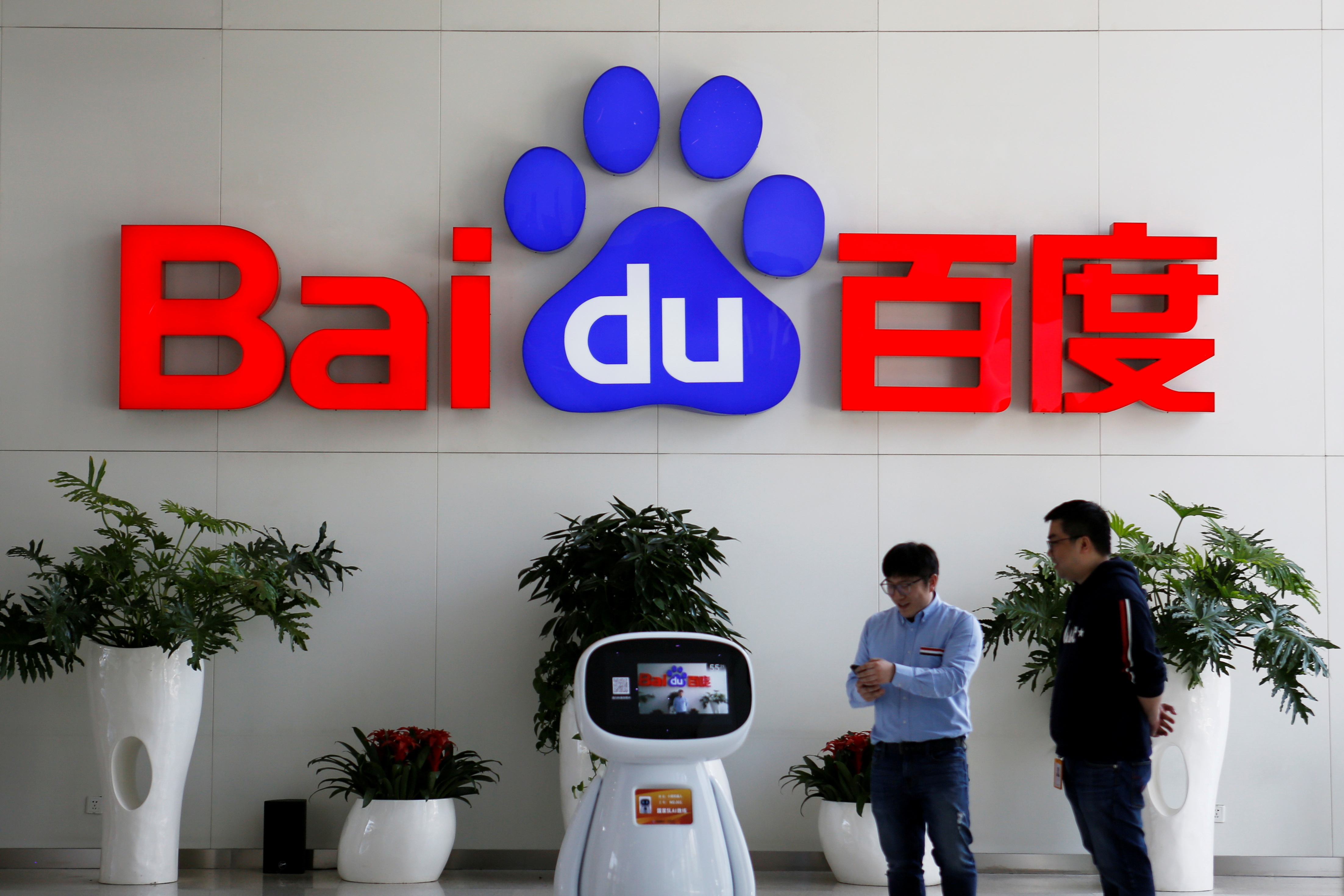FILE PHOTO: Men interact with a Baidu AI robot near the company logo at its headquarters in Beijing, China April 23, 2021. REUTERS/Florence Lo/File Photo