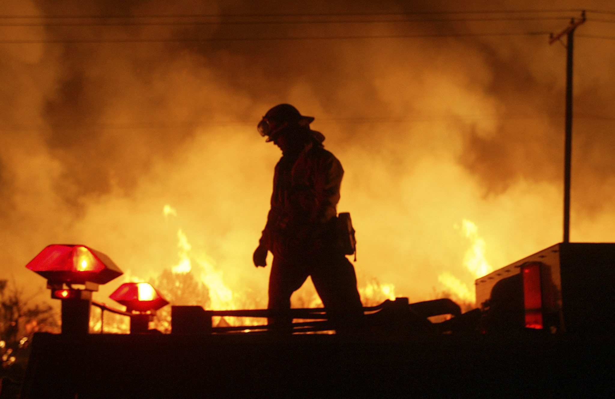 INCENDI: USA; CALIFORNIA, UN UCCELLO HA CAUSATO L'INCENDIO  A Los Angeles County firefighter walks atop a fire engine while silhouetted by flames in Acton, California late Tuesday, 20 July 2004.  The Crown Fire, in Acton, has burnt over 5,000 acres in less then 12 hours fed by high winds and superheating grasses and brush.  BRENDAN MCDERMID   ANSA-CD