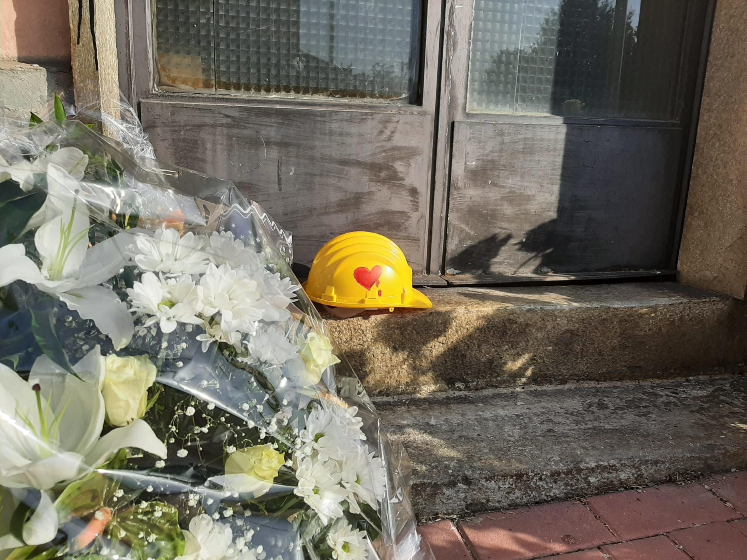 Mazzi di fori e un casco di protezione giallo, con disegnato su un lato un cuore rosso che sanguina, su di uno scalino di una porta d'ingresso della stazione di Brandizzo, nel Torinese, dove cinque operai sono morti travolti da un treno, 3 settembre 2023. ANSA/CLAUDIA TOMATIS